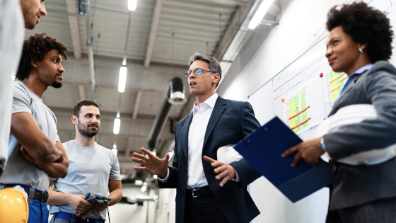 People in suit and people in workware standing in a factory site, discussing in front of a dashboard