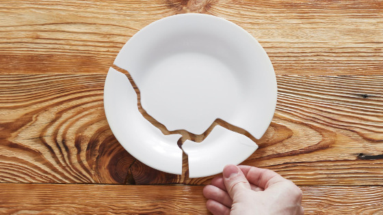 Top view on broken white plate and human hand holding one piece on wooden table