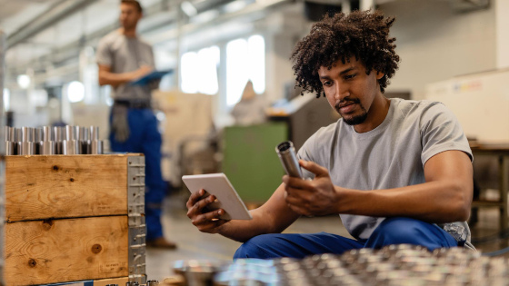 Manual worker using touchpad while examining manufactured stainless steel rods in a factory