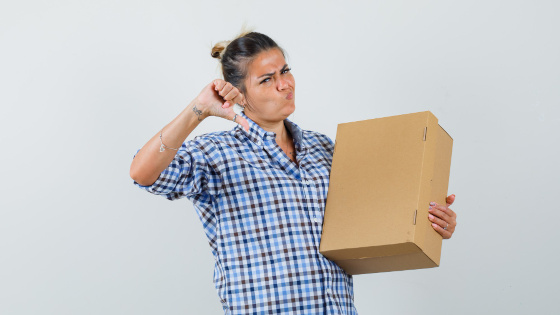 A customer holding a package holding box while showing thumb down and looking displeased